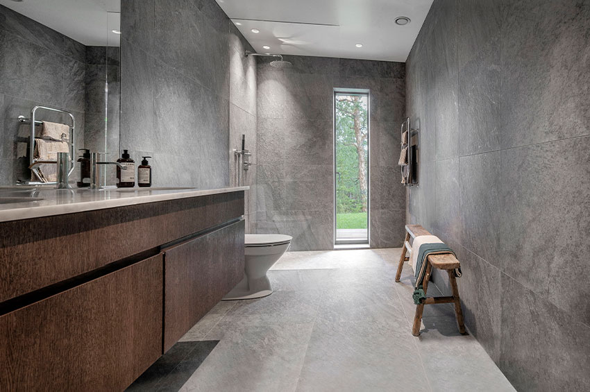 Badrum med stora grå klinkerplattor kombinerat med inredning i mörkt trä