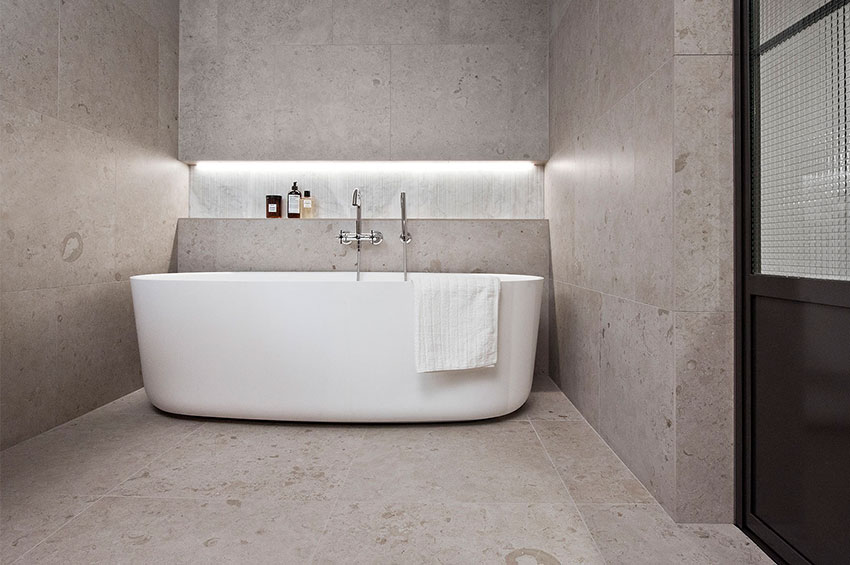 Badrum med badkar och beige/grå klinkerplattor på väggar och golv